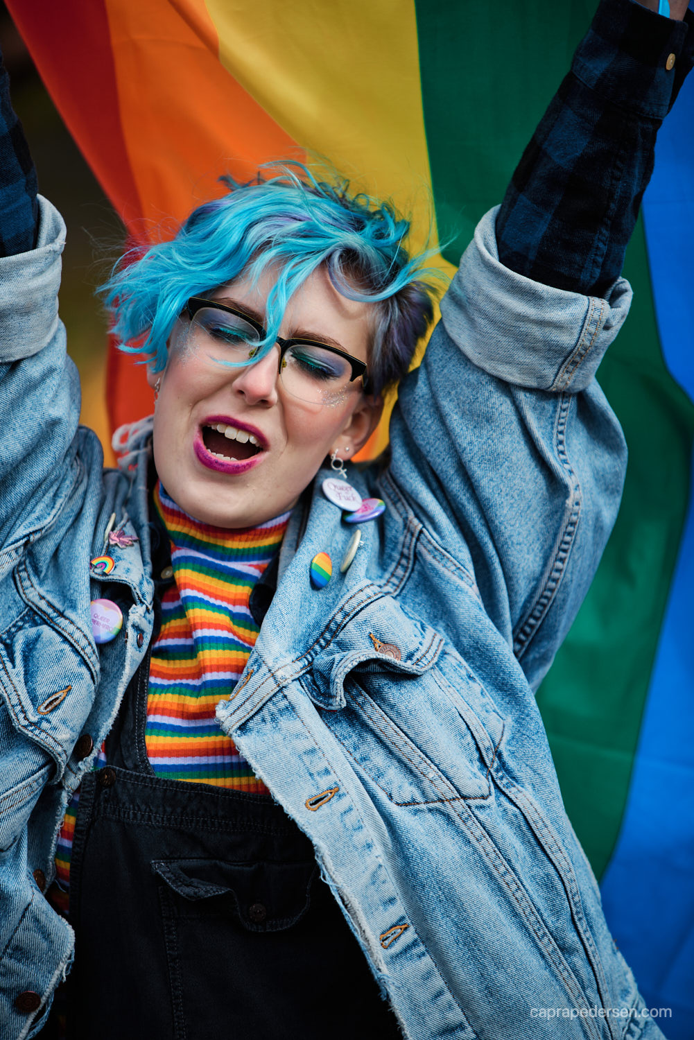 pridefestival-deltagare-med-blått-hår-under-prideflagga
