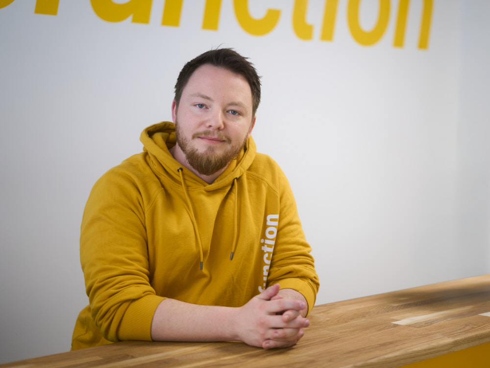 företagsfotografering-stockholm-startup-porträtt-entreprenödr-i gul-hoodie-vid-receptionsdisk